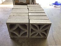Two stacks of concrete blocks displaying two distinct cutout patterns. One stack has seven blocks with floral cutouts, the other has eight with geometric cutouts.