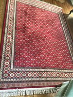 Full view of red area rug on wood floor, showing overall design, border and fringe