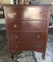 Front view of four-drawer brown wooden dresser with brass-tone ring pull hardware and turned feet.