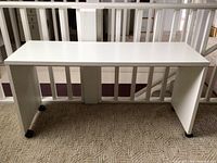 White rolling desk top on caster wheels on carpeted floor near railing.