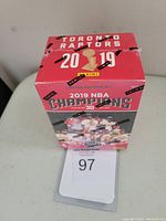 Front view of a red and black sealed 2019 Panini Toronto Raptors NBA Champions basketball card blaster box with images of players and championship trophy.
