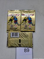 Photo of three unopened 1990 O-Pee-Chee Premiere Hockey trading card packs in gold foil packaging with hockey player images.