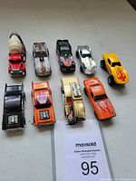 Photo showing 9 vintage Hot Wheels die cast cars arranged in two rows on a white table, displaying a variety of colors and designs, including trucks and race cars from the 1970s.