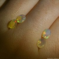 Close-up of two pairs of oval white opal gemstones placed on skin to demonstrate size and color play.