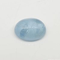 Close-up photo showing the oval cabochon blue aquamarine gemstone with light blue hue and surface reflections.