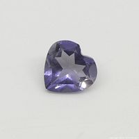 Close-up image of a heart-shaped violet-blue iolite gemstone on a white background showing clarity and cut details.