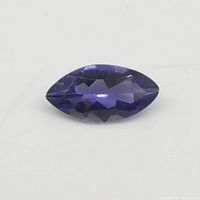 Close-up image of the marquise-shaped violet-blue iolite gemstone showing its facets and color on a white background.