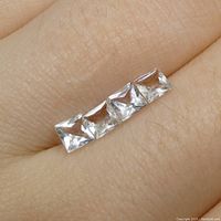 Close-up photo of four square-cut aquamarine gemstones on a finger showing size and clarity.