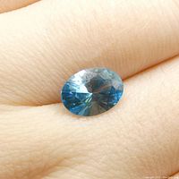 Top-down view of the oval blue zircon gemstone on a finger to show scale and color.
