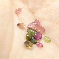 Multiple natural tourmaline cabochon gemstones in varying pink and green hues laid in a hand for size reference.
