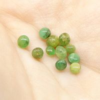 Close-up photo showing 12 small sphere green emerald gems held in palm, displaying natural inclusions and color variation.