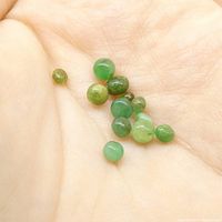 Twelve small spherical green emerald gemstones arranged on the palm of a hand showing size and color variations.
