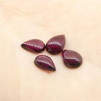 Four pear cabochon rhodolite garnet gemstones resting on a person's palm, showing size and color