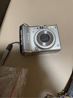 Front view of a silver Canon PowerShot A520 digital camera showing lens, flash, and wrist strap on a tan surface.