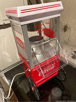 Photo of Coca-Cola branded popcorn machine showing glass sides, red and white colors, tilt-down front door, and wheels.