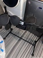 Full view of Ion electronic drum machine with four black square drum pads and control panel mounted on metal frame with carpet flooring background.