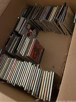 Photo showing a box partially filled with rows of CDs stacked vertically, viewed from above.
