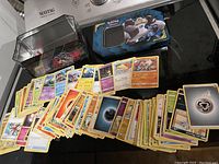 Photo showing Pokémon trading cards spread out with Pokémon-themed metal tin case featuring Galarian Rapidash.
