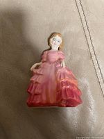 Photo of Royal Doulton bone china figurine depicting a young woman in a pink and red tiered dress, set on a beige background.