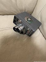 Vintage Versa Dial camera positioned on a light beige leather chair, showing the body, dual lenses, and control dial on top.