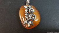 Front view of the amber pendant showing the polished amber surface and sterling silver rose and leaf decorations with the 925 clasp.