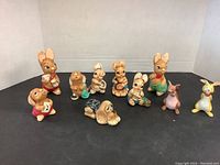 10 animal figurines on black surface with white backdrop, showing variety of bunnies, a dog, a kangaroo, mouse, and rabbit with musical instruments and accessories.