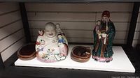 Wide view of two ceramic figures and small wooden trays on shelf