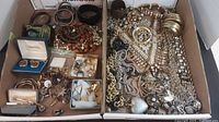 Two trays filled with assorted men's costume jewelry including cuff links, tie pins, rings, bracelets and necklaces in various metal tones and bead styles.