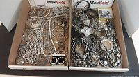Two cardboard trays filled with assorted silver-colored costume jewelry including bracelets, necklaces, earrings, pendants in various designs and sizes