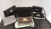 Overview of seven black and glittery small evening clutches, arranged on a table with some resting on a striped cloth bag.