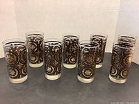 Eight matching gold and black highball tumblers arranged in two rows