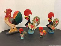 Group photo showing all five rooster figurines arranged by size and style on a black surface.