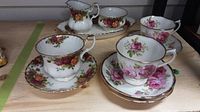 Full view of 5 cups and saucers plus cream jug, sugar bowl, and tray showing floral patterns and gold trim.