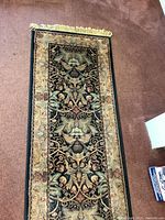 Full view of the Jordan's area runner rug placed on a carpeted floor, showing overall design and fringed edges.