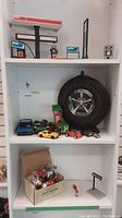 Esso gas station playset and toy cars on shelving with large black tire and box of toy figures below