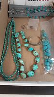Overview of the turquoise jewelry lot including various necklaces, a bracelet, rings, and a bag of loose stones.