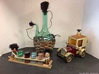 Full view of vintage wine carafe in rattan holder, wooden shooter glass holder with troll figurines, and vintage car-shaped carafe