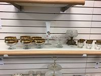 Full shelf view showing all items: gold-rim dessert glasses, shooter glasses, frosted vase, candy dish on brass stand, and two-tier tray.
