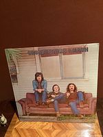 Front cover of sealed Crosby, Stills & Nash 1st album showing band sitting on a couch in front of a window; photo taken to show album condition and seal.