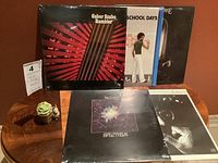 Five sealed jazz vinyl albums with titles visible including Gabor Szabo Rambler, Stanley Clarke Journey to Love and School Days, and Billy Cobham Spectrum and Shabazz. Albums are arranged standing and laying down on a wooden table.