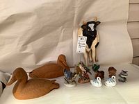 Photo showing all items in the lot including resin ducks, wooden cow, swan salt and pepper shakers, bisque birds and molded animal figures arranged on a white backdrop.