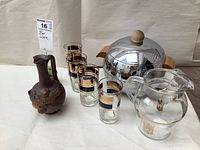 Photo showing all items including chrome Westbend Penguin ice bucket with lid, Wisers Rye pitcher and four matching glasses, and Artisan Calvados ceramic pitcher.