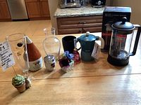 Front view of all items on table showing Bodum French press in box, blue espresso maker, vintage beer glass, various ceramics and glassware