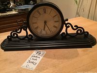 Front view of the battery operated metal and plastic mantel clock showing clock face with Roman numerals and decorative base.