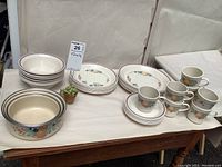 Photo showing eight dinner plates, eight side plates, eight bowls, eight mugs with saucers arranged on table with fruit pattern