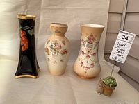 Three Crown Devon vases, two cream-colored with floral designs and one black with red berry decorations and gold trim.