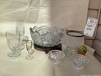 Overall view showing cut crystal bowl, candle holders, liqueur glass, etched grape wine glass, champagne flute, ice bucket with metal rim, all arranged on light background.