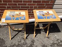 Front view of two matching new Cortona natural wood folding tray tables with labels on top.