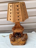 Front view of hand carved wooden folk art lamp showing the couple seated by the fireplace and the woven wood shade.