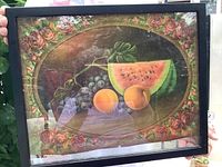 Photo of framed lithograph showing an oval still life of southern fruits with rose border, held up to show wear and antique condition